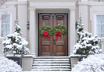 Front door of stucco house with colorful Christmas wreath and elegant wooden double door