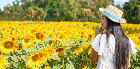 Young female tourist wearing a wicker hat happily stand in a sunflower field.