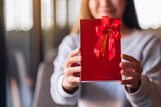 Closeup image of a beautiful young asian woman holding and showing a red present box