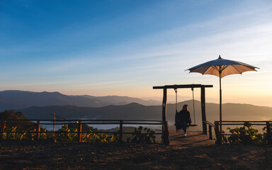 A female traveler sitting on a swing while watching a beautiful view and sunrise in the morning
