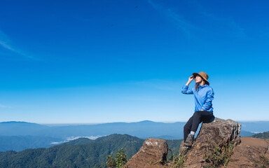Naklejka na ściany i meble A female traveler hiking and sitting on mountain peak, looking at a beautiful view