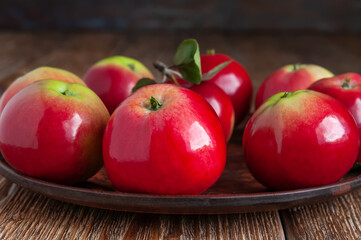 Ripe organic apples on a ceramic dish on a dark wooden table.