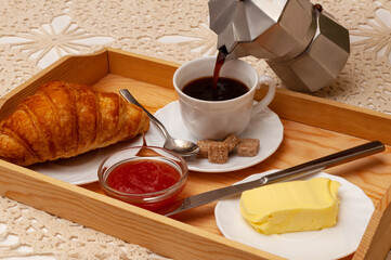 Breakfast with croissant, coffee, jam and butter served on the wooden tray