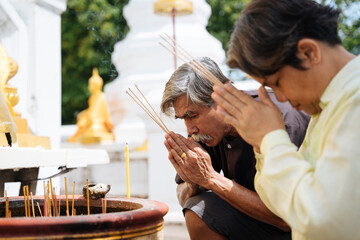 Asian senior elderly couple holding incense pay respect in thai temple.