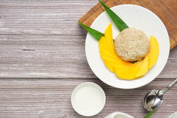 Top view of Thai dessert, Mango Sticky rice with coconut milk on wooden background, copy space juicy mango dessert