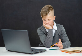 Pensive teen boy uses laptop at school. Distance education concept