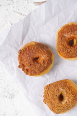 Donat or Donut or Doughnut as circle with hole sweet bread topped with caramel and biscuit crumbs. Pile of doughnut in white shiny background