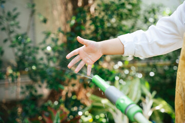 Hand of kid watering plant with pipehose in garden.