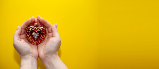 Female hands on a yellow background hold a Christmas tree toy in the form of a heart