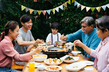 Asian family enjoy eating BBQ together outdoor at park.