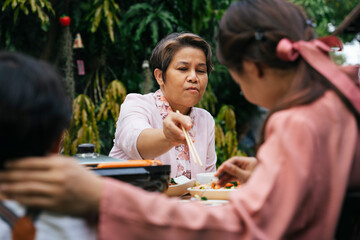 Senior eldery woman using chopstick eating food in dining party outdoor.