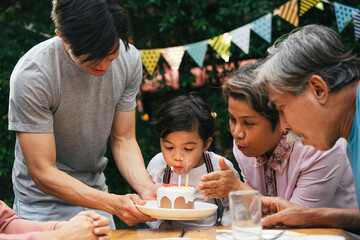 Asian family celebrate birthday party for a kid with cake at yard.