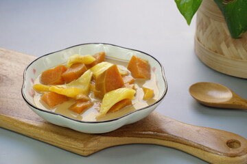A plate of Kolak Ubi Nangka or Indonesian dessert made from Sweet Potato and Jack fruit as a compote. Based on coconut milk, palm sugar and Pandanus leaves in isolated gray background