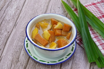 A bowl of Kolak Ubi Nangka in wooden table. Kolak is an Indonesian dessert based on palm sugar, coconut milk, and pandanus leaf contains Sweet Potato and Jack fruit or Banana