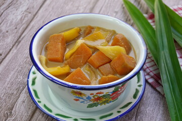 A bowl of Kolak Ubi Nangka in wooden table. Kolak is an Indonesian dessert based on palm sugar, coconut milk, and pandanus leaf contains Sweet Potato and Jack fruit or Banana