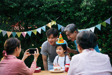 Asian kid celebrate birthday party with family outdoors.
