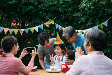 Asian kid celebrate birthday party with family outdoors.