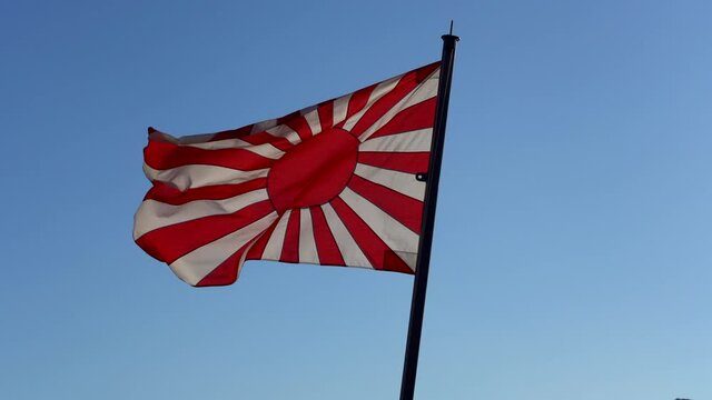 Rising sun flag waving in the wind against the blue peaceful sky. japan military banner