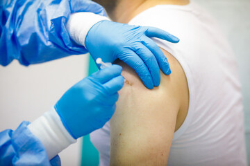 Details with a man getting an intramuscular injection with the Sars-Cov-2 vaccine in a hospital from a medical worker.