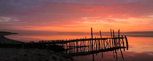 Tranquil seascape with jetty silhouette and dramatic red sky at dawn.