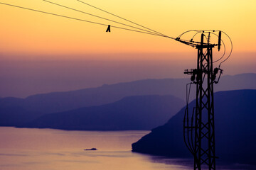 Fototapeta na wymiar High voltage towers on coast at sunset