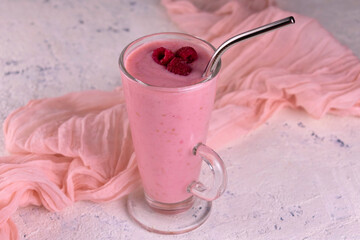 Raspberry smoothie in a tall glass on a white table.