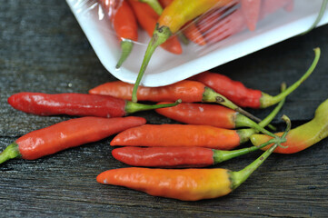 Some red chilies on a black wooden base and a bunch of red chilies in a plastic box