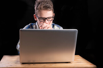 Boy with shirt and glasses holds hands in front of face in front of laptop