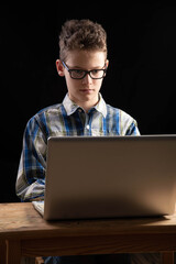 Boy with shirt and glasses makes home schooling on laptop