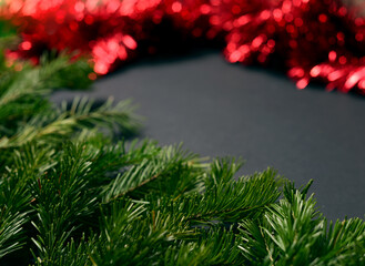 Black background with fir branches on the left corner and red tinsel to decorate the Christmas tree on the right.
