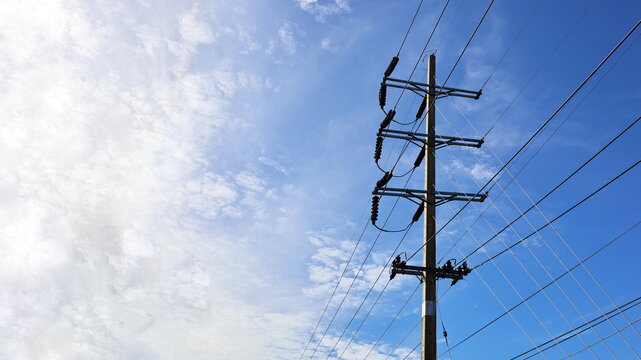 Power transmission lines on concrete poles. High and low voltage cables with insulators and guy wire to support the pole. On the sky background with morning sun with copy space. Selective focus