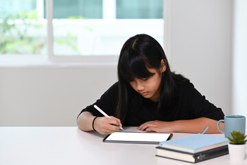 A schoolgirl using digital tablet doing homework online at home. Online education, learning at home, homeschooling concept.