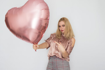 Blonde woman holding big pink heart balloon in her hands