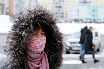 Coronavirus protection, woman in medical mask and fur hood standing on winter city street. Concept of illness, fever, cold and flu
