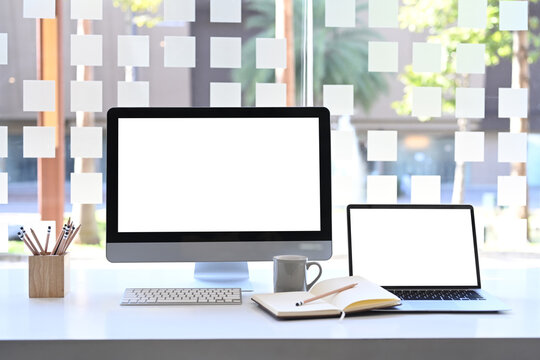 Front view of modern workstation with blank screen computer and laptop on white table.