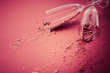 Two champagne glasses with splash of red heart shaped confetti on red background