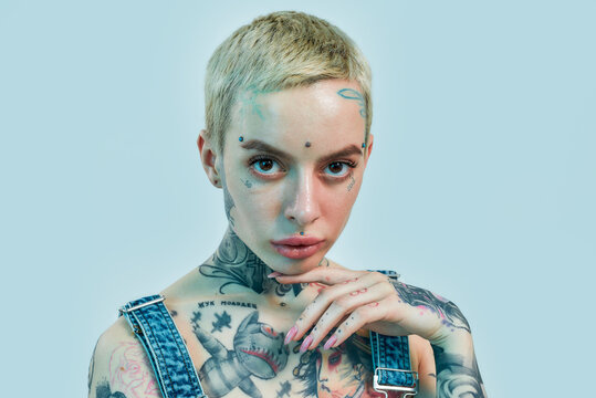 Tattoo and piercing. A close up of a white tattooed woman with piercing having her palm close to her face with her head tilted slightly and looking into a camera