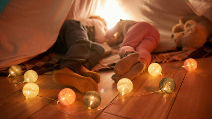 Sweet dreams. Two little children falling asleep while lying on a blanket in a hut made with bedsheets at home © Svitlana