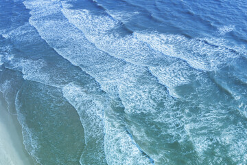 Seascape. Sandy beach. Sea waves roll onto the sandy beach. Top diagonal view. Abstract nature landscape background