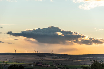 Horizontal view of a sunset in the countryside with wind mills in the background with a small cloud and rain in the background