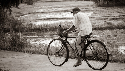Old man cycling in the streets of a rural village sepia tone photograph,