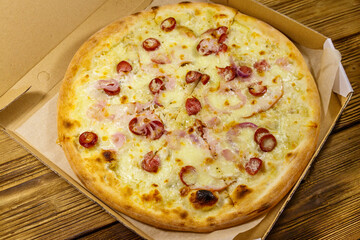 Delicious fresh pizza in cardboard box on a wooden table. Concept for home delivery of food, fast food, delivery of pizza