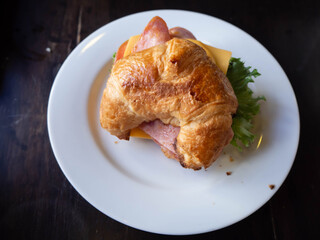 Ham and Cheese Croissant in a white plate on a wooden table.