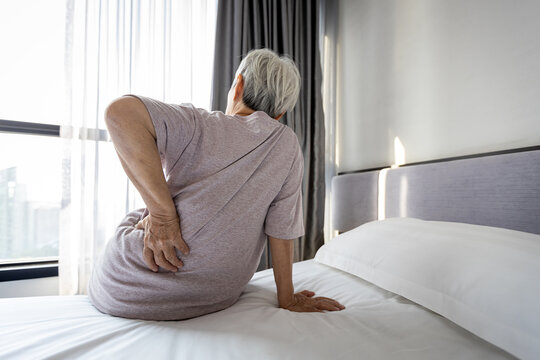 Stressed asian senior woman suffering from backache,sitting on bed massage her waist pain,unhappy old elderly people waking up in the morning after sleeping on uncomfortable mattress or bad posture