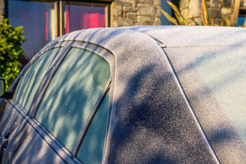 detail of a frozen car covered with thick layer of ice on cold winter day, suburban house  in...