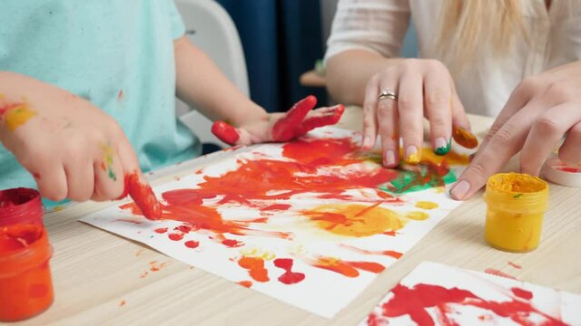 Closeup of adult and child drawing with hands and fingers using colorful paint on white paper. Concept of creative education and art skills development