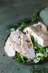 Turkey breast stuffed with vegetables and cheese served with green mix salad and aromatic herbs, green stone background.