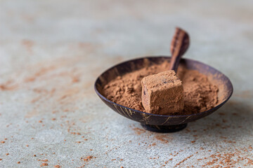 Dark chocolate truffle sprinkled with cocoa powder and cocoa powder in wooden bowl, light concrete background.