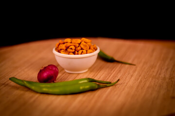 Masala or spicy shing , is a very popular Gujarati snack, white bowl,masala shing Namkeen or roasted spicy peanuts on wooden table with onion and green chili