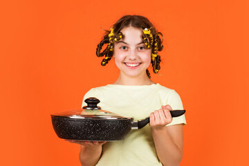Stereotype housewife style. Small girl with curlers in hair. Pin up style. Girl hold Frying Pan....